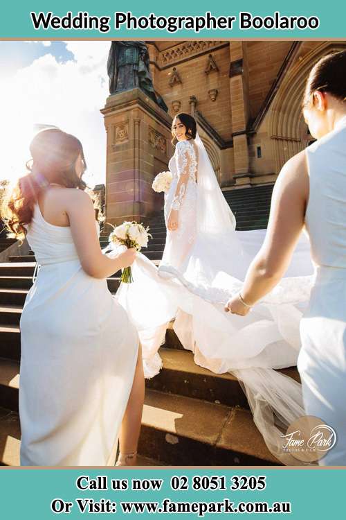 Photo of the Bride smiling on the bridesmaid holding the tail of her wedding gown at the front of the church Boolaroo NSW 2284